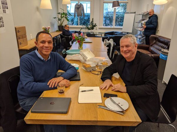Two men sitting at a table with laptops.