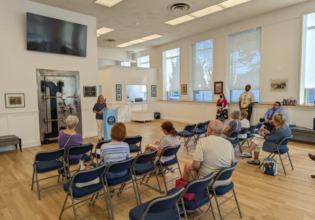 9ebbb9e164cc6e18bf94a772cde0f184 A group of people sitting in chairs inside a room.